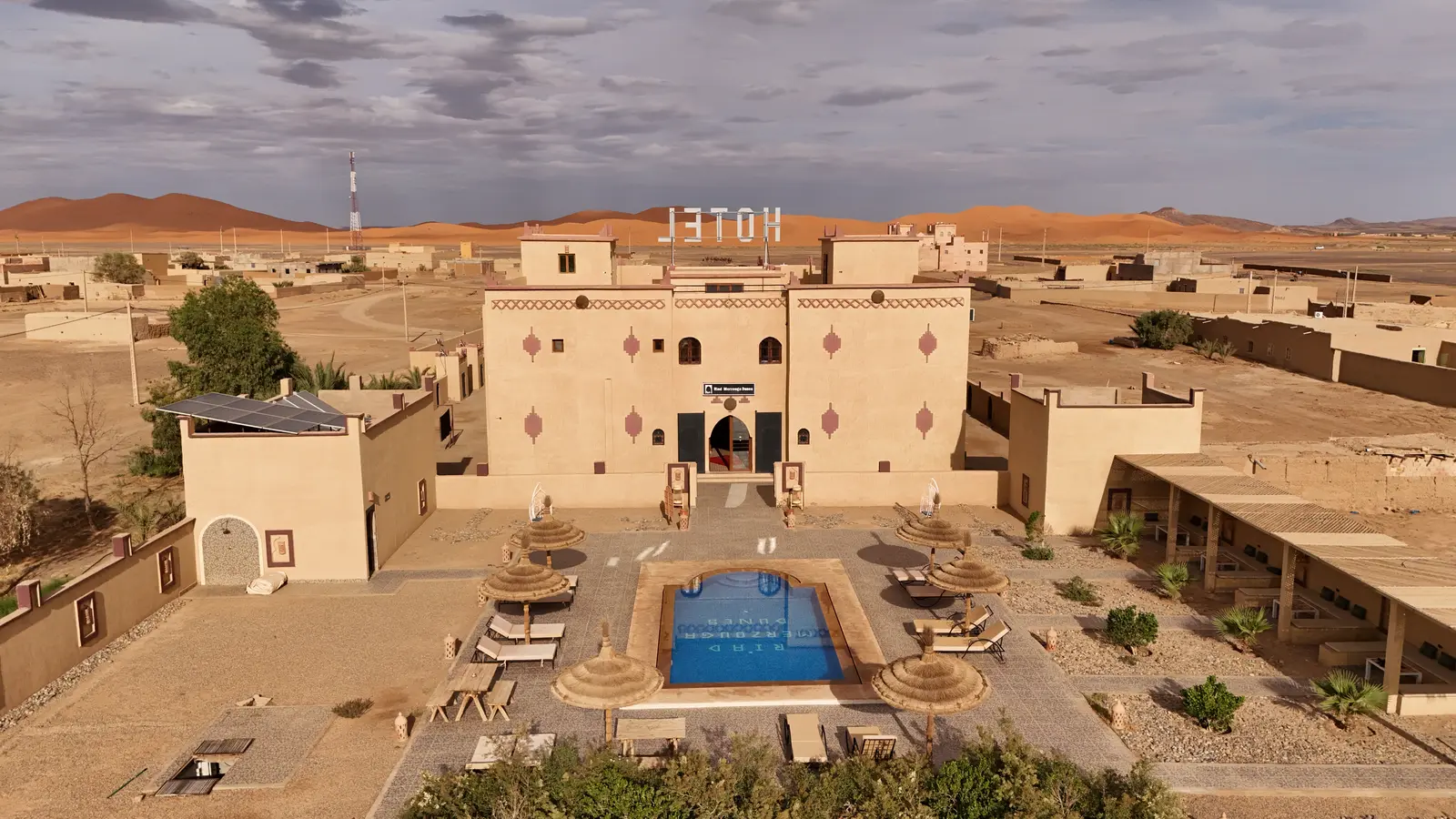 Aerial view of Riad Merzouga Dunes with its pool and garden, the Erg Chebbi dunes on the horizon